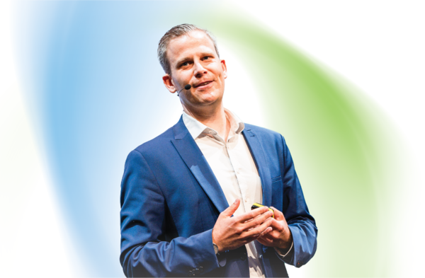 Philipp Pfister, Sector Vice President at Transporeon, a Trimble Company, speaks while wearing a blue suit and headset microphone against an abstract blue and green background.