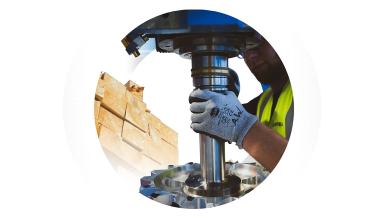 Nahaufnahme der behandschuhten Hände eines Arbeiters, der ein industrielles Metallbauteil hält, vor dem Hintergrund gestapelter Holzbalken, eingerahmt von einer Kreisgrafik.