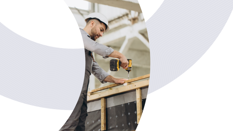 A worker in a hard hat and grey workwear uses a power drill on a wooden frame to demonstrate Portakabin’s manufacturing process.