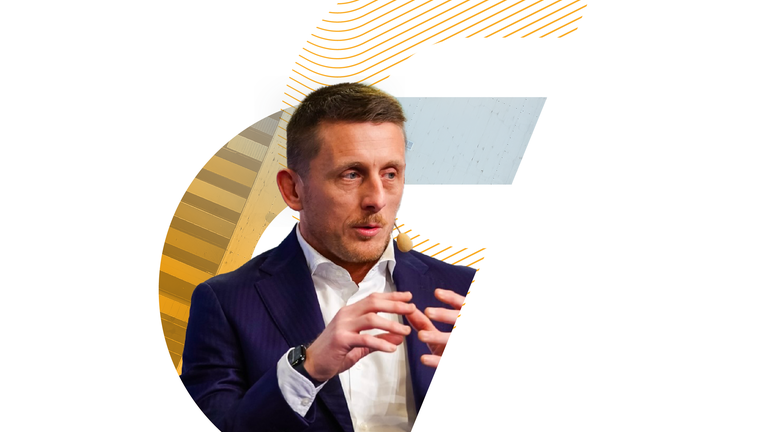 Un professionista in abito che parla con un microfono ad archetto, posizionato all'interno di una cornice grafica con motivi a linee gialle.